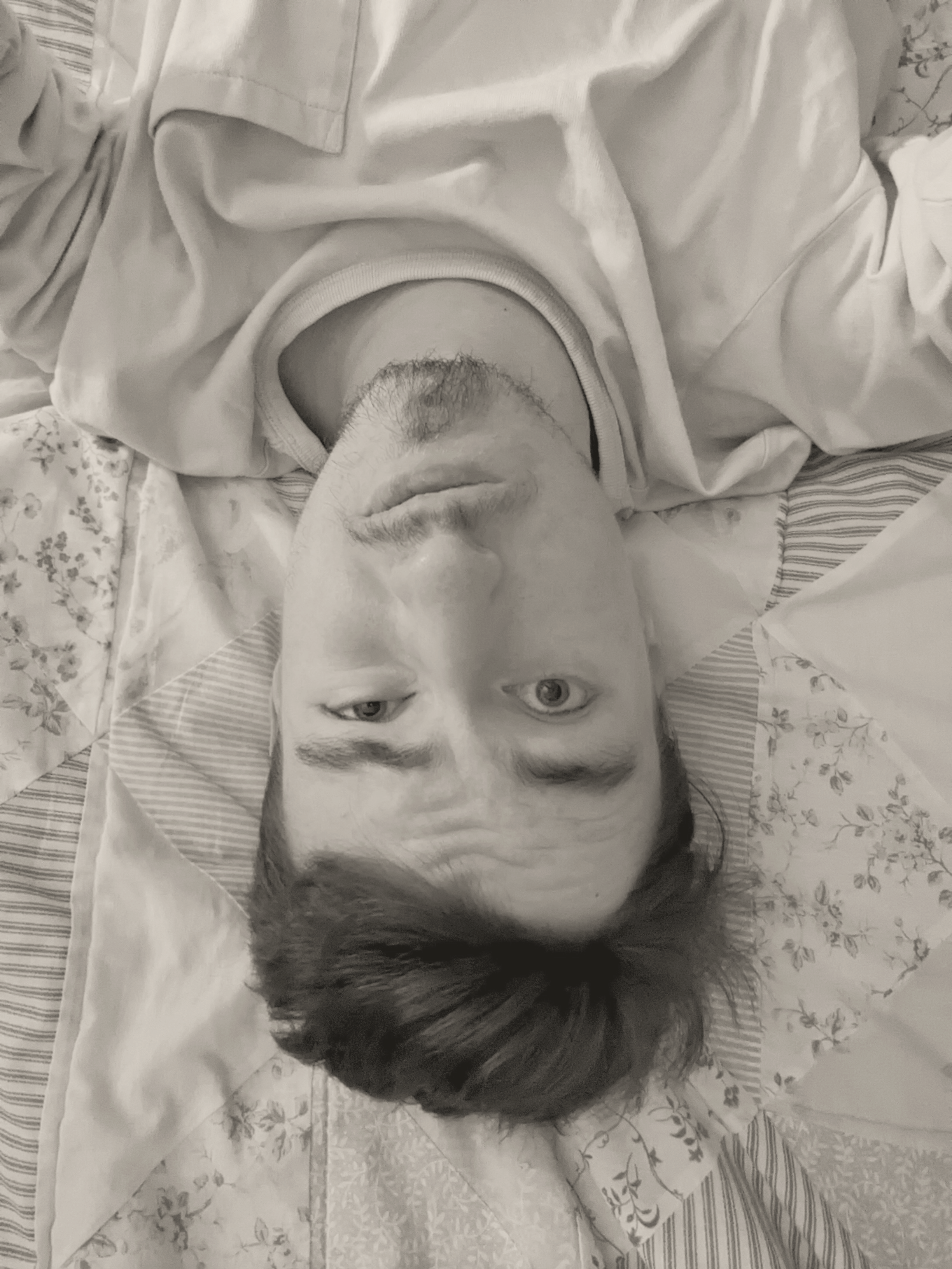 A selfie of me laying upside-down on a quilt while making a weird face.